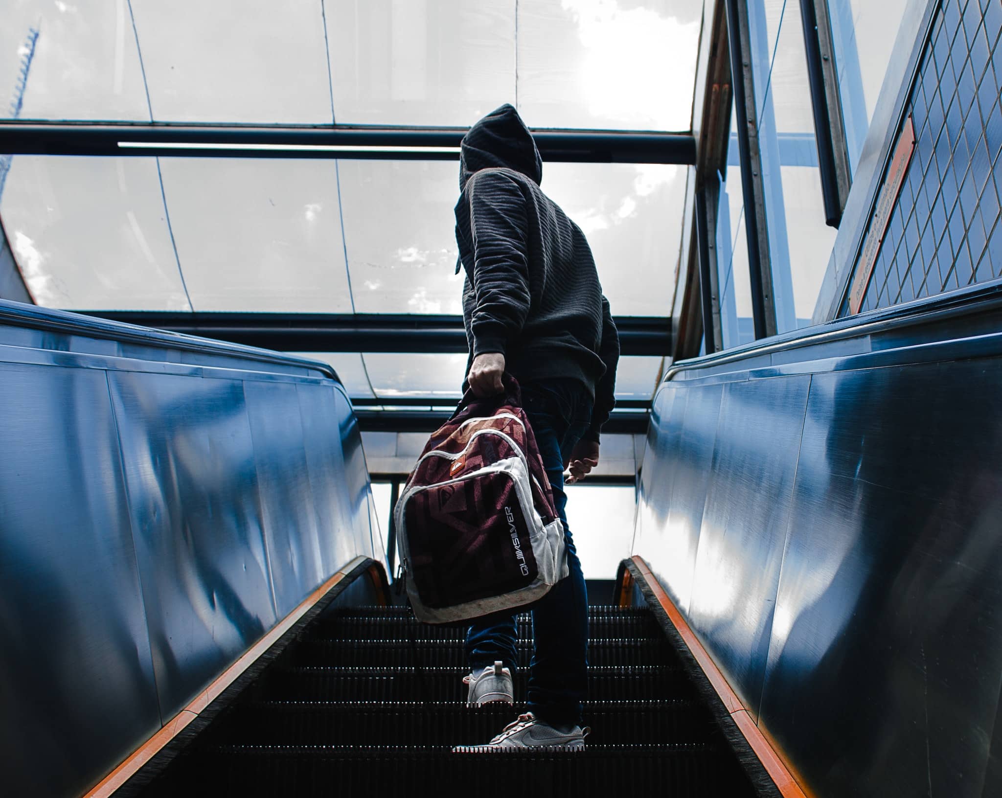 Person Wearing Black Hooded Jacket Standing on Escalator While Holding Backpack